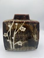 Front view of square Japanese ceramic vase with dark brown glaze and white floral branch design on the front face.