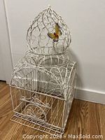 Front view of the large white ornamental birdcage showing detailed metalwork and butterfly accent.