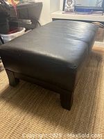 Side view of large black faux leather poof with visible texture and solid legs.