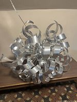 Front view of the mid-century modern style chandelier showing aluminum curled ribbons creating a spherical shape on a wooden surface.