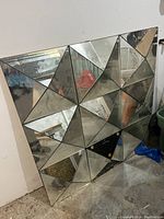 Front full view of large geometric wall mirror showing triangular mirrored panels with some aging marks and one panel missing.