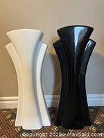 Front view of two large vases, one white and one black, showing their wide, fan-like shapes and glossy surfaces.