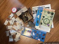Photo of the starter rock and mineral collection including boxed specimens, labeled bags, booklets, and charts spread on a wooden floor.