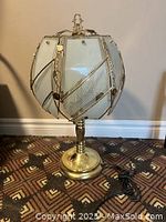 Front view of Tiffany style table lamp showing brass base and shaped glass shade with decorative metal framing and etched glass panels.
