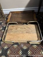 Two wooden trays on patterned carpet: one darker wood tray with built-in handles, one lighter wood tray with metal handles