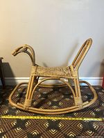 Side view of the vintage rattan horse rocker illustrating woven seat, curved rocker base, and horse head and tail handles.