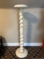Full view of white pedestal plant stand showing twisted column, round base and top platform against an indoor wall.