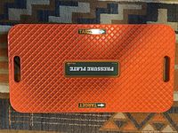 Top view of orange WhyGolf Pressure Plate with diamond textured surface and target markings shown on carpet.