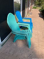 Side view of stacked green and blue Adirondack chairs showing slatted design and armrests.