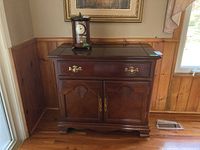 Full view of wooden cabinet against paneled wall with a clock on top.