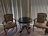 Two embroidered armchairs and a decorative round wooden table between them, showing floral and figurative embroidery on upholstery.