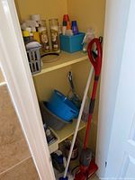 Photo of cleaning closet showing red-handled mop, blue and gray buckets, plunger, and cleaning items on shelves