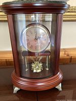 Close-up front view of the quartz mantel clock showing clock face, wooden frame, glass panels, and metal elements