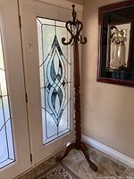 Full view of wooden coat stand positioned near a glass door, showing height and hook arrangement.