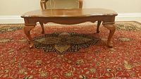 Side view of a wood coffee table showing ornate carved legs and curved edges, placed on a patterned rug.