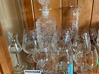 Full view of crystal brandy decanter, brandy glasses, additional glassware, and vase arranged on a table.
