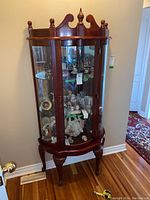 Front view of wood framed curio cabinet showing glass shelves and door with decorative top.