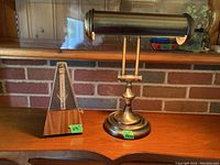 Brass desk lamp and wooden metronome on wooden surface with brick background