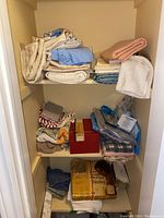 Photo of closet shelves with folded linens including towels, tablecloths, cloth face masks in plastic bags, and a red box likely containing heating pad.