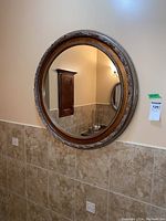 Full view of round mirror mounted on wall above tiled backsplash and reflecting part of the room.