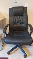 Front view of black vinyl office chair with padded seat and backrest on castors.
