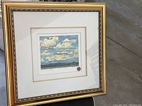Framed print titled Summer Clouds showing a textured cloud sky over landscape, signed and numbered 158/495 with red embossed seal.
