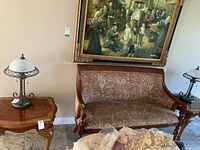 Side table shown beside patterned wooden framed couch with lamp on top