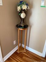 Full view of the wooden plant stand with round black top holding the decorated vase with faux flowers in a room corner.