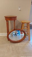 Wood stool, oval mirror with wood frame, and partially visible wooden stool against a beige wall on tile flooring