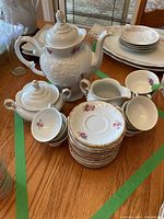 Full tea set arranged on wooden table including teapot, sugar, creamer, cups and saucers with floral design and gilded trim.