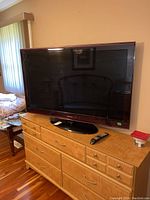Full view of Samsung 52-inch TV on wooden dresser with remote on dresser.
