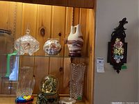 Glass vases, decorative covered dishes on shelf, pottery vase, nativity water globe, floral wall art