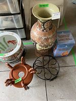 Wide shot of decorative tall vase with painted horse-drawn carriage scene, Himalayan salt lamp box, two metal bases, and a porcelain planter with koi fish design.