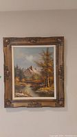 Full image of the framed landscape painting depicting mountains, trees, and water.
