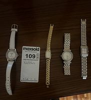 Five watches laid out flat on a wooden surface showing variety in band materials and face shapes.