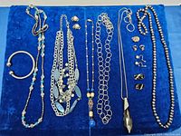Full view of the jewelry collection showing six necklaces, one bracelet, and several pairs of earrings on a blue cloth.