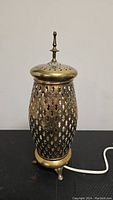 Full frontal view of brass pierced lantern-style table lamp showing lattice pattern, finial on top, and small three-footed base