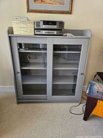 Front view showing grey cabinet with two glass sliding doors and items on top.