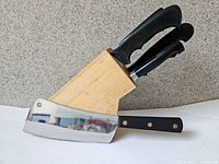 Full view of Sabatier cleaver lying in front of a wood knife block holding multiple black handled knives