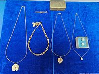 Overview of all necklaces, link chain bracelet, earrings, and brooch on blue background