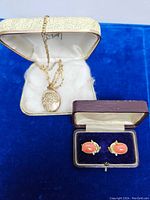 18kt gold necklace with locket in cream-colored vintage case and pair of earrings in brown case on blue surface