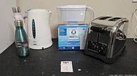 Full view of all items: Hamilton Beach toaster, Braun kettle, Brita filter box, two insulated travel drink bottles