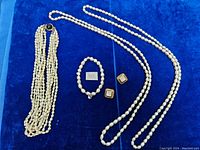 Photo of full lot showing multi-strand pearl necklace, two single-strand pearl necklaces, bracelet, and earrings on blue velvet background