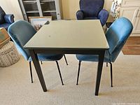 Front view showing square solid wood table with glass top and two blue upholstered chairs around it.