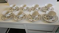 Eight porcelain cups and saucers arranged in two rows on a white table, showing the full set from the front