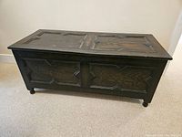 Full front and side view of the closed dark wood chest showing carved front panel with geometric patterns.