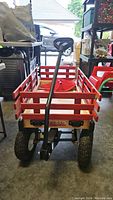 View of red wooden wagon from rear showing black pull handle and pneumatic tires.