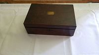 Closed antique wooden writing box with dark wood finish and a metal lockplate on the front.