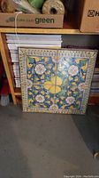 Front view of the 4 ceramic tiles arranged square with colorful floral and yellow geometric design.