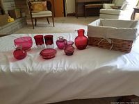Wide view of all cranberry glass items arranged on white surface with basket in background